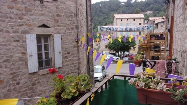 Una calle estrecha con edificios de piedra, un cartel de 'Office de Tourisme' y plantas en macetas en los balcones.