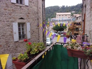 Una stretta via con edifici in pietra, un cartello con la scritta 'Office de Tourisme' e vasi di piante sui balconi.