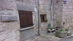 Un edificio de piedra con una ventana con persianas de madera, una puerta pequeña y una planta en maceta en el suelo.
