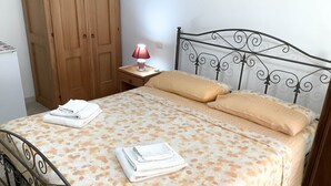 Ein ordentlich bezogenes Bett mit Blumenmuster, zwei Kissen und gefalteten Handtüchern auf einem Metallgestell mit Kopfteil.