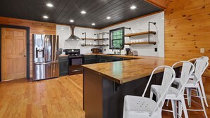 A modern kitchen with wooden accents, stainless steel appliances, and a central island with bar stools. - Mountain View Luxury Lodge! Movie Theater, Hot Tub, Fire Pit! (Blue Ridge)