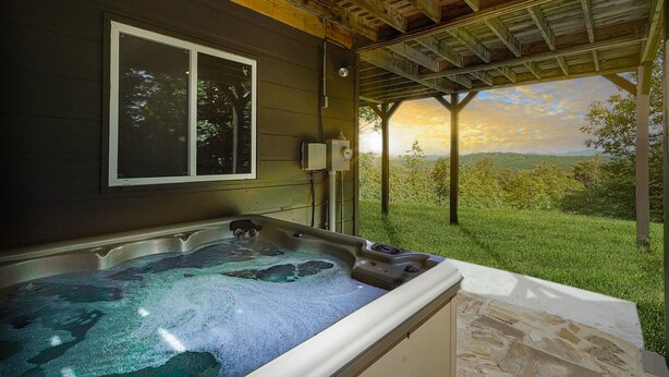 A hot tub in a covered outdoor area with a view of a grassy landscape and a sunset. - Mountain View Luxury Lodge! Movie Theater, Hot Tub, Fire Pit! (Blue Ridge)