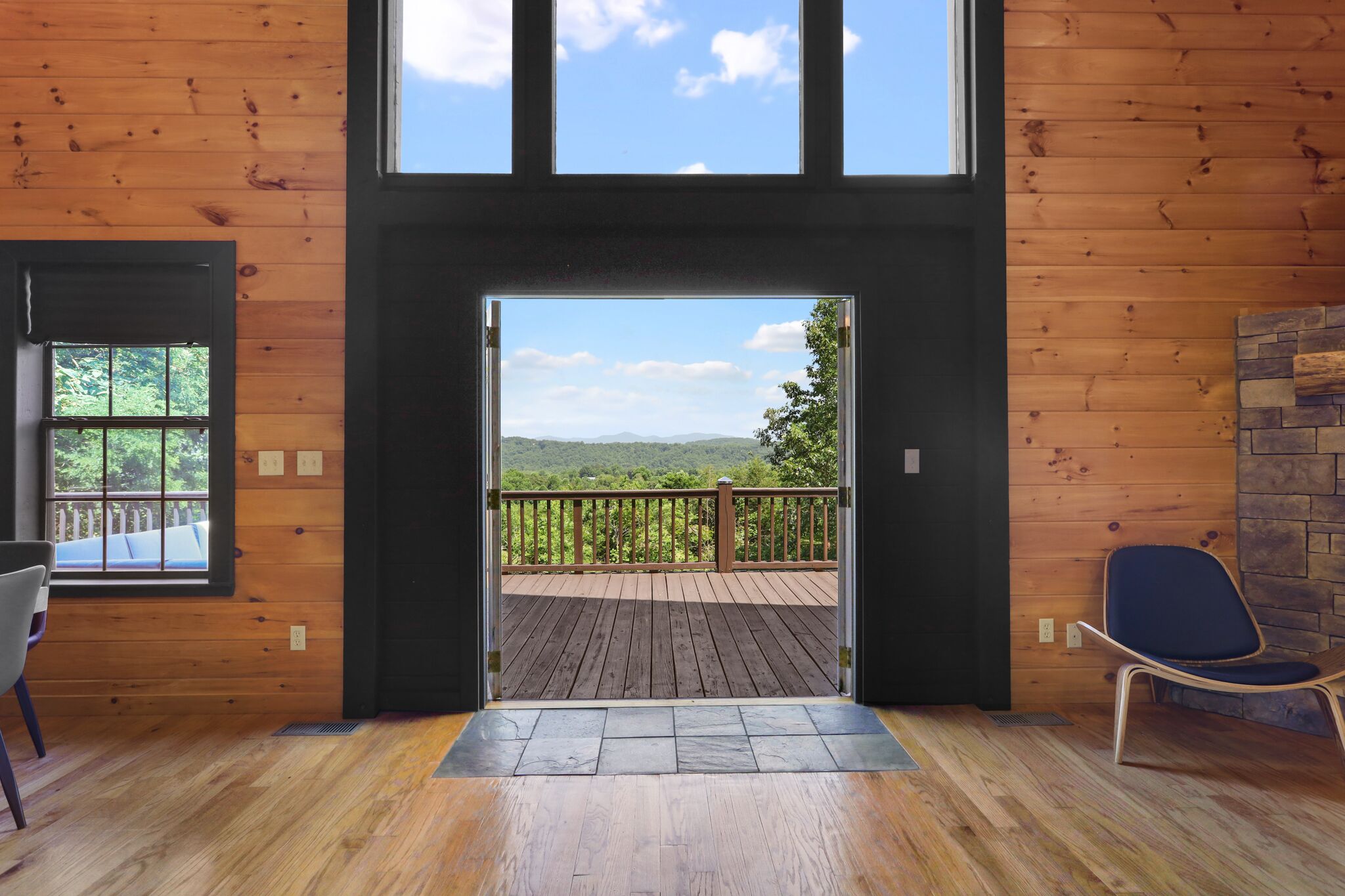 A wooden interior with a large window and door leading to a deck with a view of the mountains.