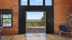 A wooden interior with a large window and door leading to a deck with a view of the mountains. - Mountain View Luxury Lodge! Movie Theater, Hot Tub, Fire Pit! (Blue Ridge)