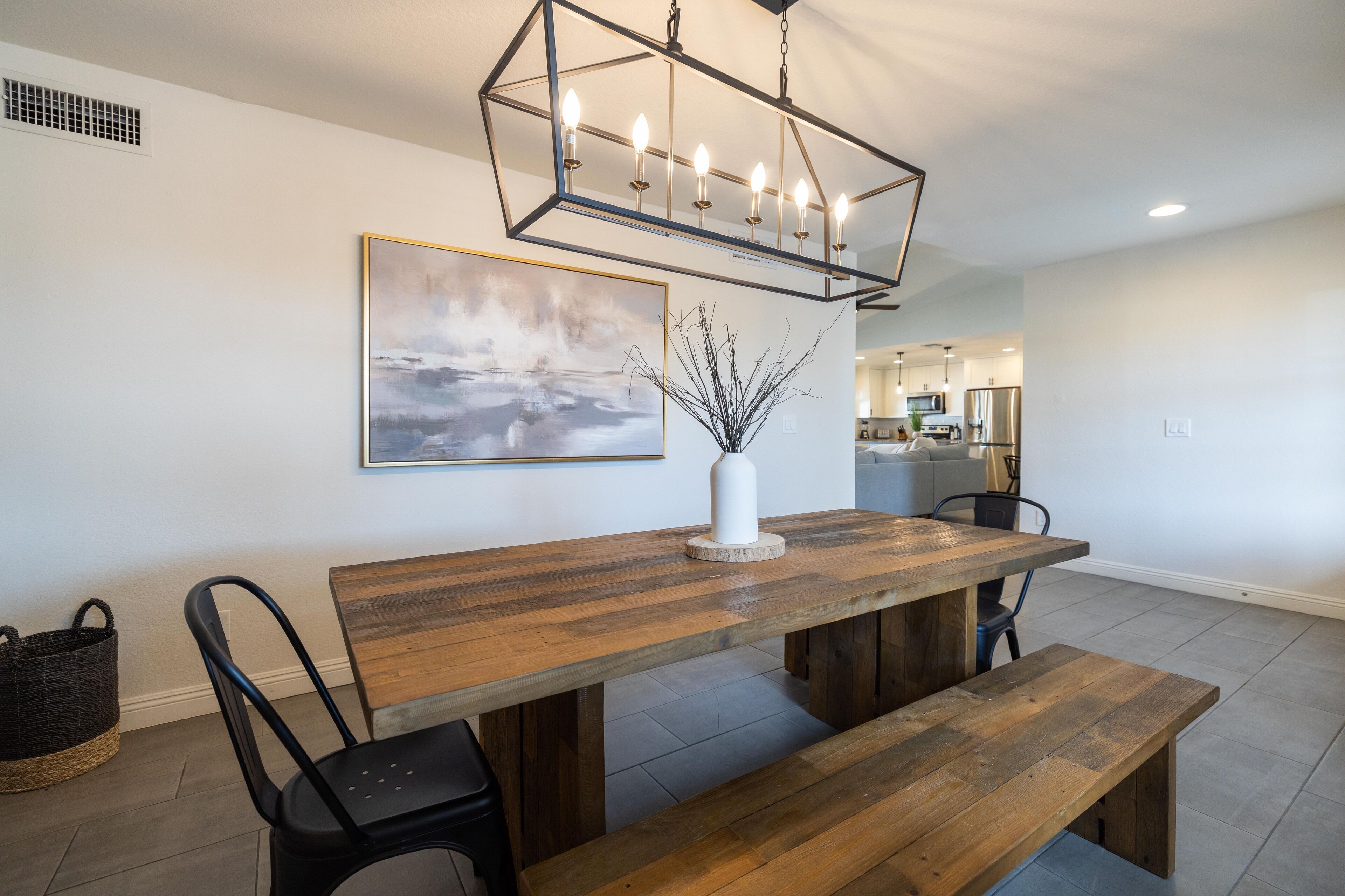 A dining area with a wooden table, black chairs, a bench, a hanging light fixture, and a painting on the wall.