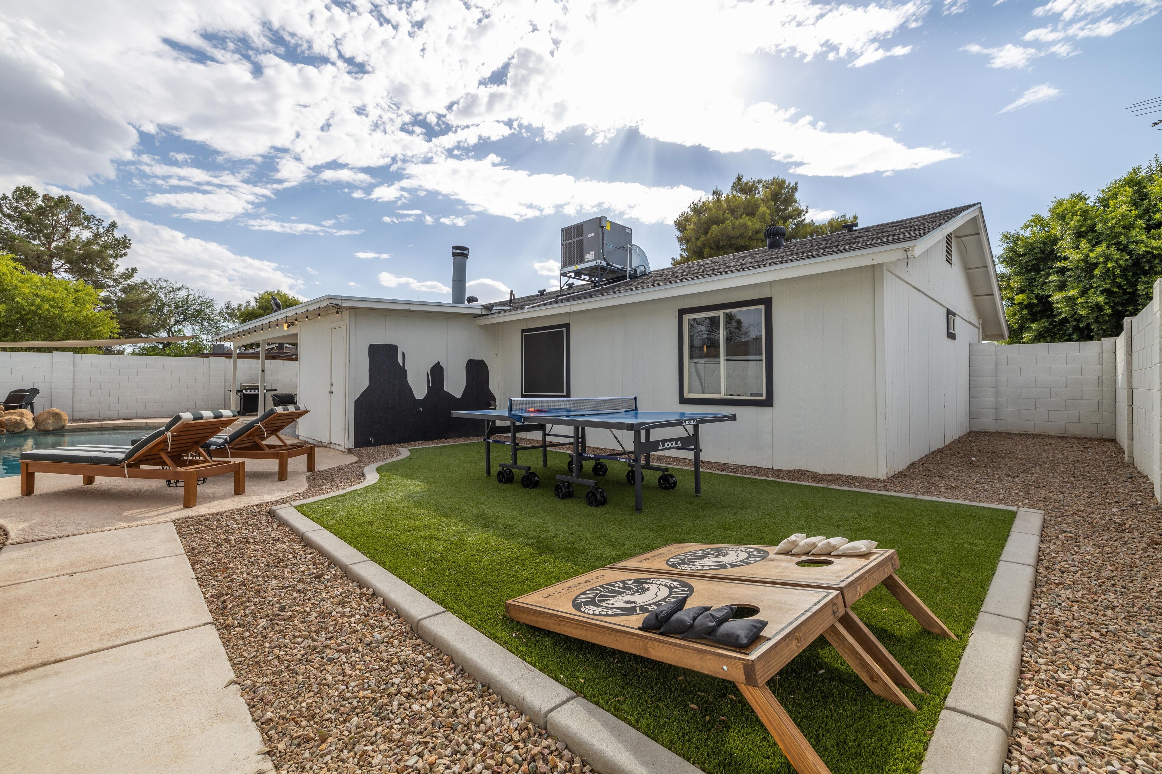 A backyard with a pool, lounge chairs, a ping pong table, and a wooden table with stones.