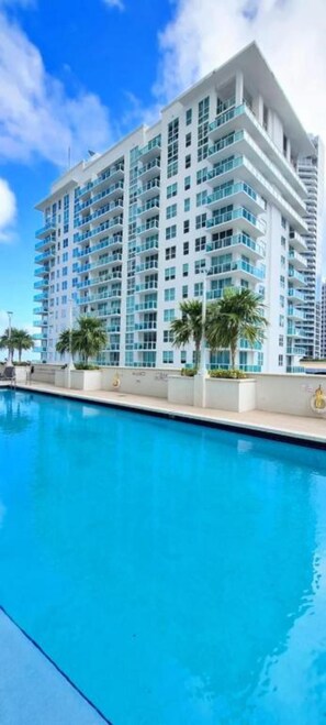 A modern multi-story hotel with a pool in the foreground.