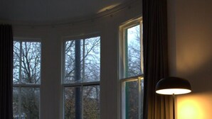 Camera d'albergo con un letto, una sedia, un tavolo e una lampada. Tre finestre offrono luce naturale.