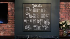 Un’area bar con una lavagna che elenca cocktail, poltrone in pelle e un camino.