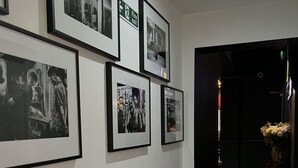 Un corridoio con fotografie in bianco e nero incorniciate alle pareti, una segnaletica di uscita di sicurezza e una porta che conduce in un'altra stanza.