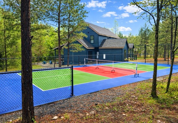 A tennis court with a fence, trees, and a building in the background.
