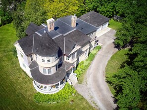 A large, multi-story house with a circular tower, a driveway, and lush greenery surrounding it.