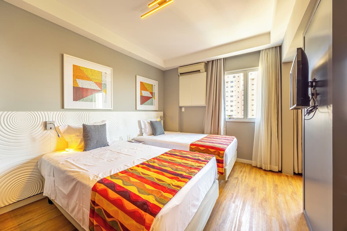 Une chambre d’hôtel avec deux lits, une télévision et des œuvres d’art accrochées aux murs.