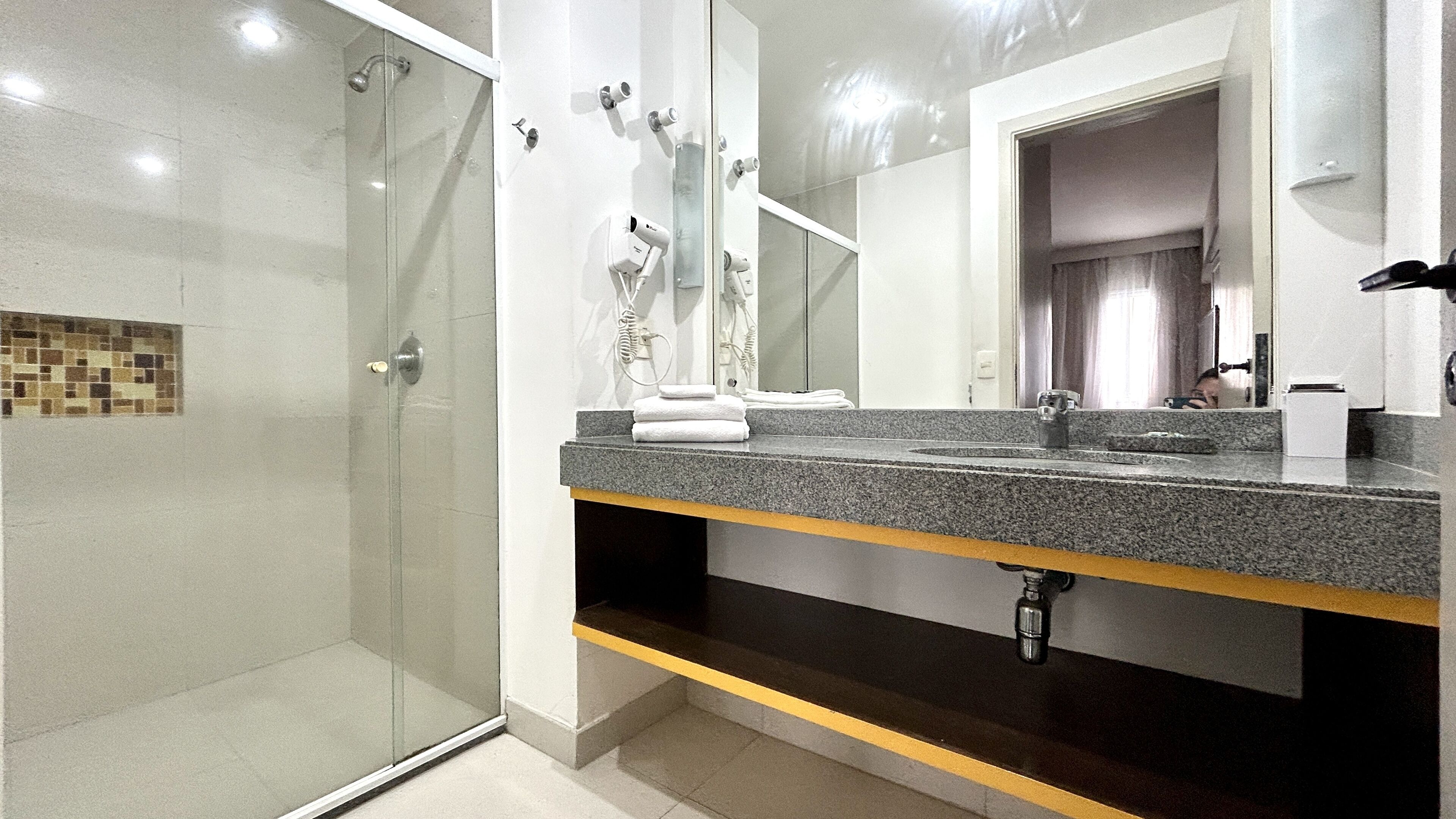 Un baño moderno con cabina de ducha de vidrio, un espejo grande y encimera de granito.