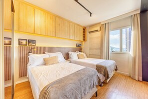 Habitación de hotel con dos camas, paneles de madera, una ventana con cortinas y vista a la ciudad.