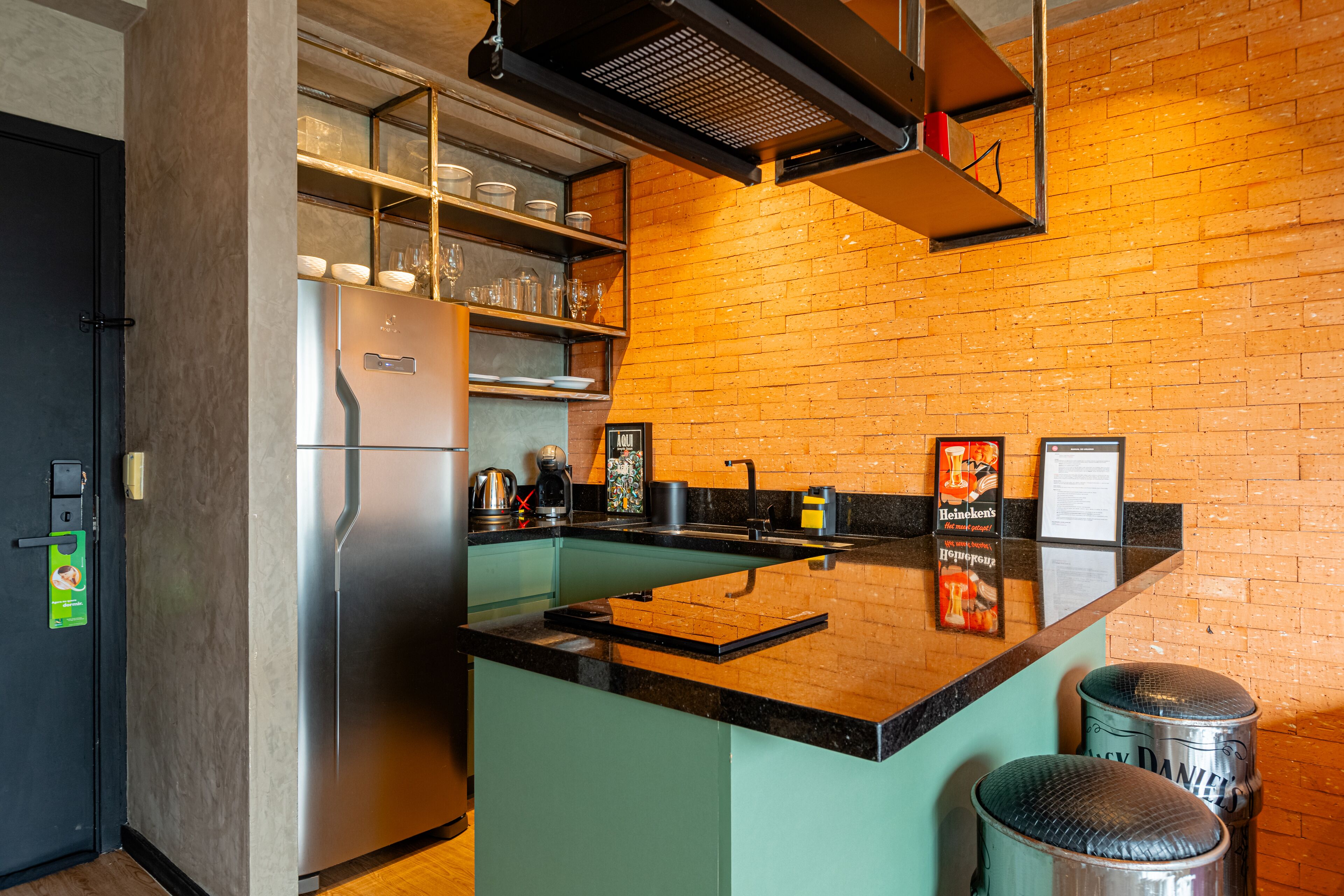 A kitchen with a stainless steel refrigerator, a sink, and a coffee machine. There are stools and a shelf with glassware.