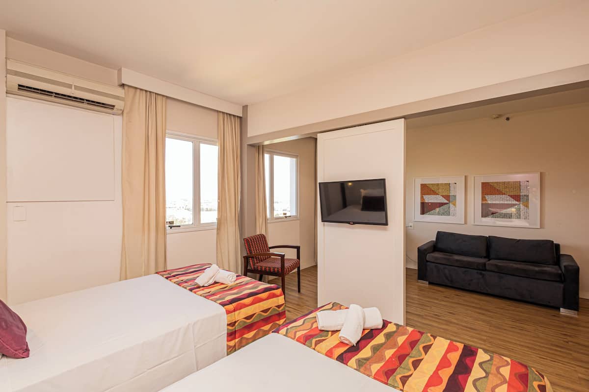 Une chambre d’hôtel avec deux lits, un canapé, une télévision et des œuvres d’art accrochées au mur.