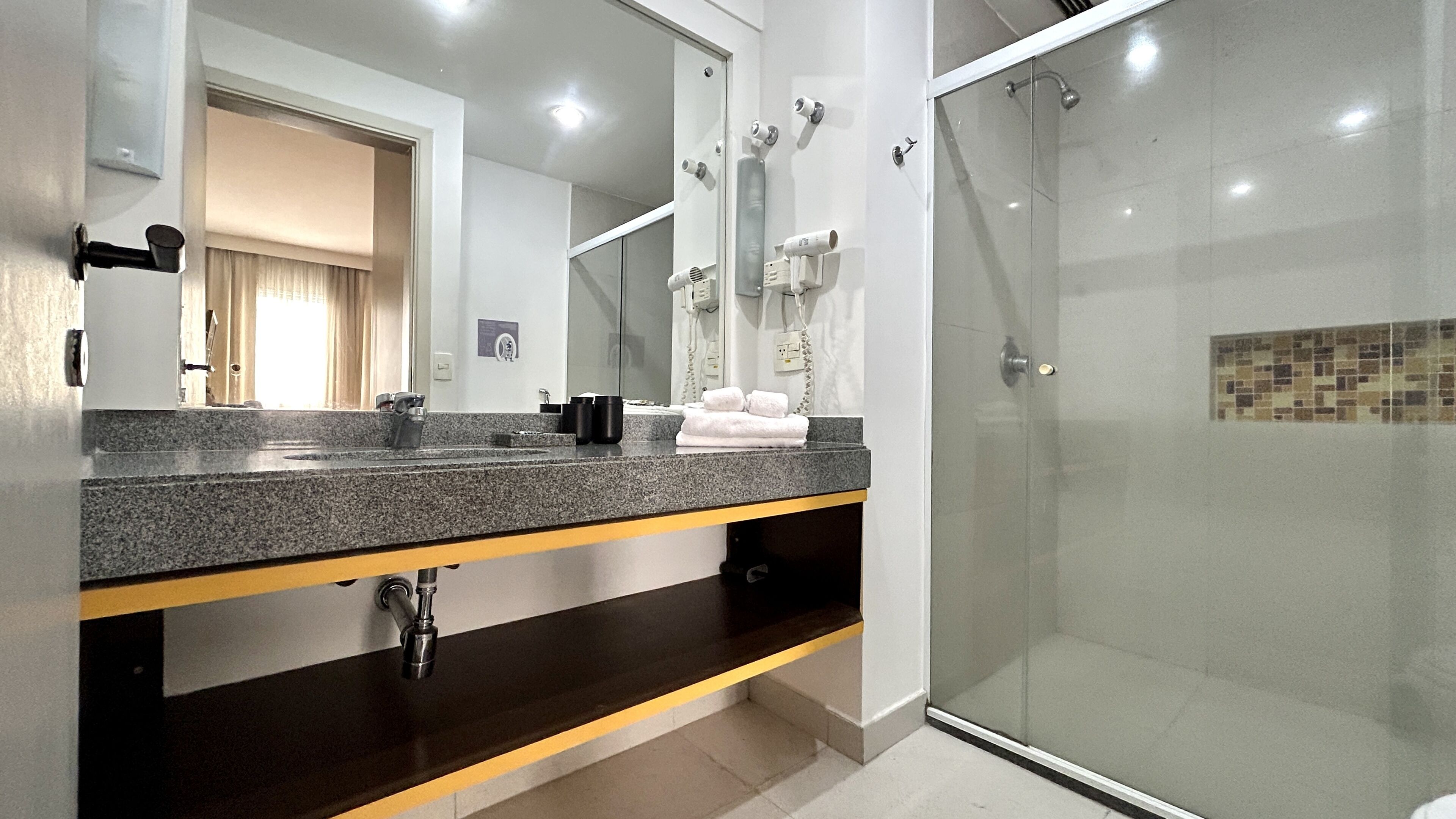 Un baño moderno con encimera de granito, cabina de ducha con vidrio y espejo con toallero.