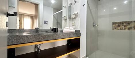Un baño moderno con encimera de granito, cabina de ducha con vidrio y espejo con toallero.