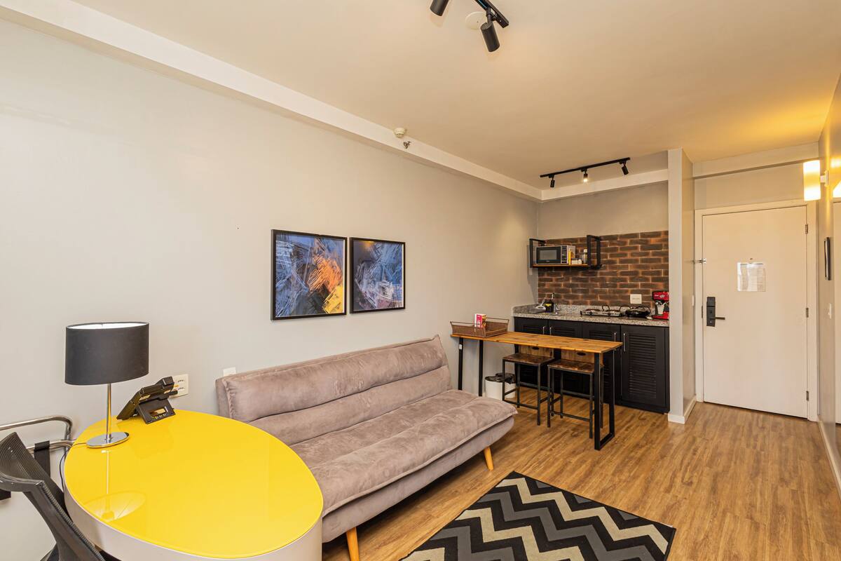 Un espace de vie compact comprenant un canapé, une table jaune, un coin cuisine et une porte.