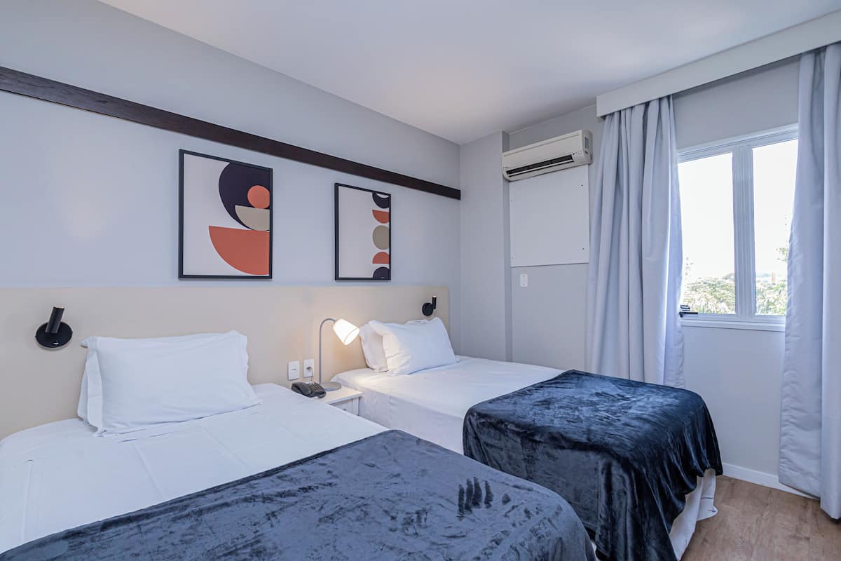 Une chambre d’hôtel avec deux lits, une table de chevet, une lampe et des œuvres d’art accrochées au mur.