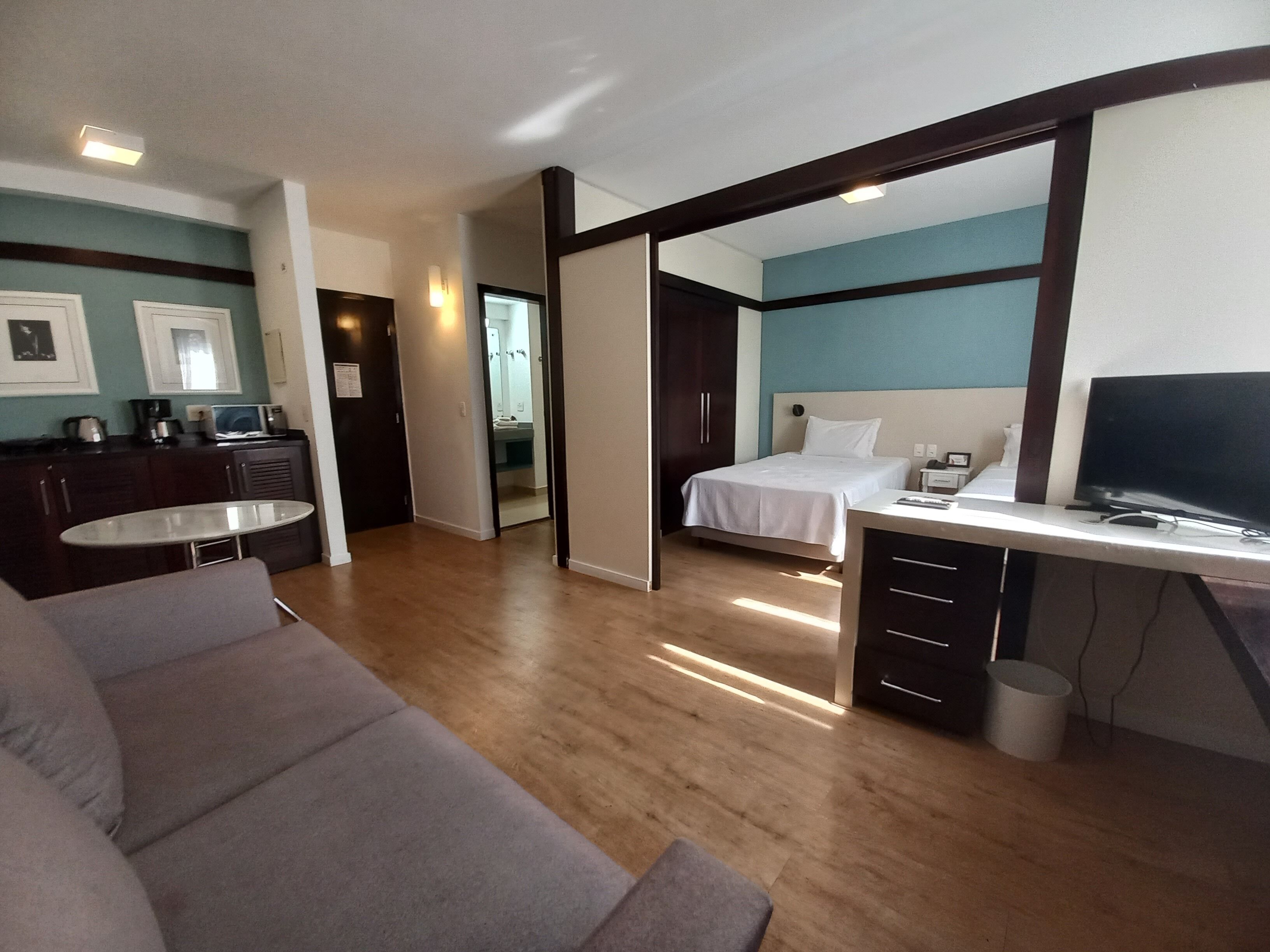 Een moderne hotelkamer met een bed, een bureau met een televisie, een bank en een kitchenette.