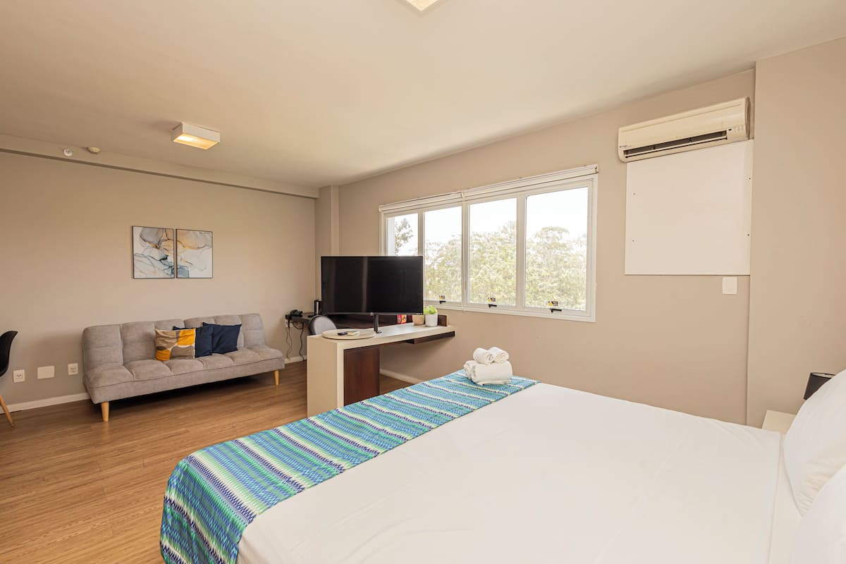 Une chambre d’hôtel avec un lit, un bureau avec une télévision, un canapé et une fenêtre.
