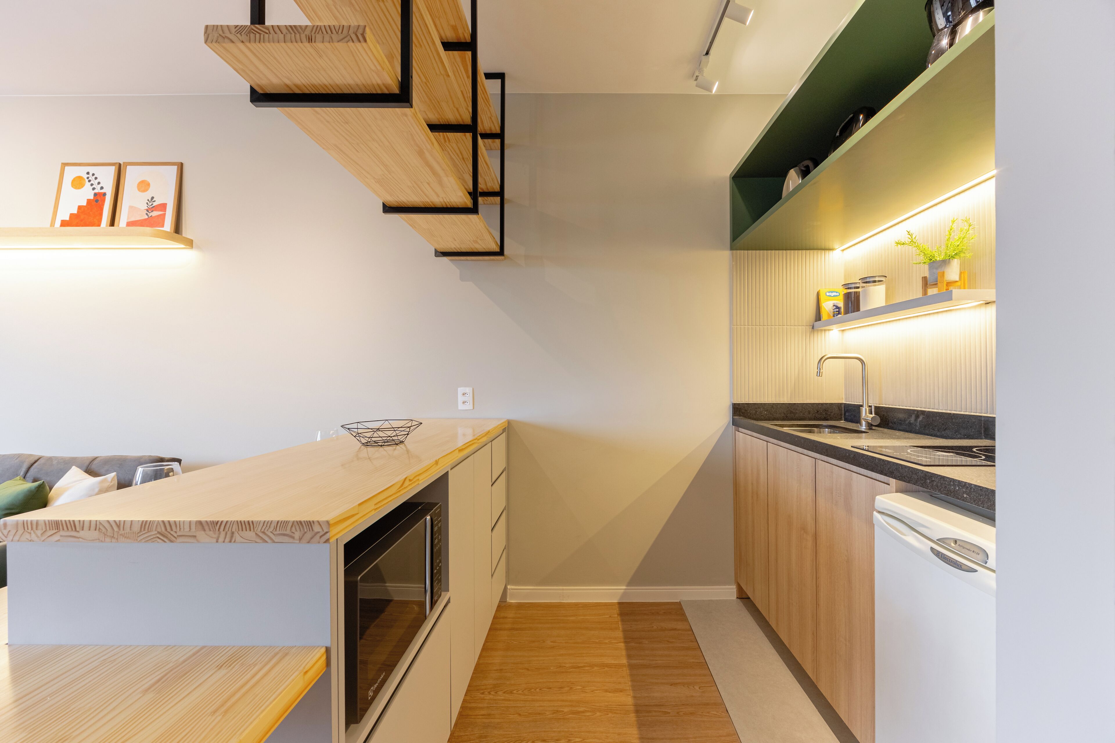Una cocina moderna con muebles de madera, horno empotrado y lavavajillas. Hay cuadros en la pared y una encimera con un cuenco.
