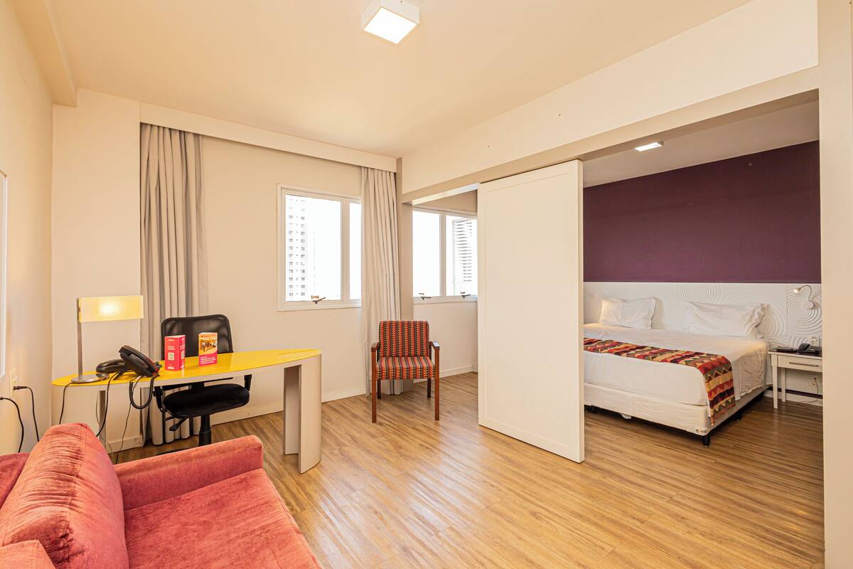 Une chambre d’hôtel comprenant un lit, un bureau avec une chaise, un canapé et une fenêtre avec des rideaux.