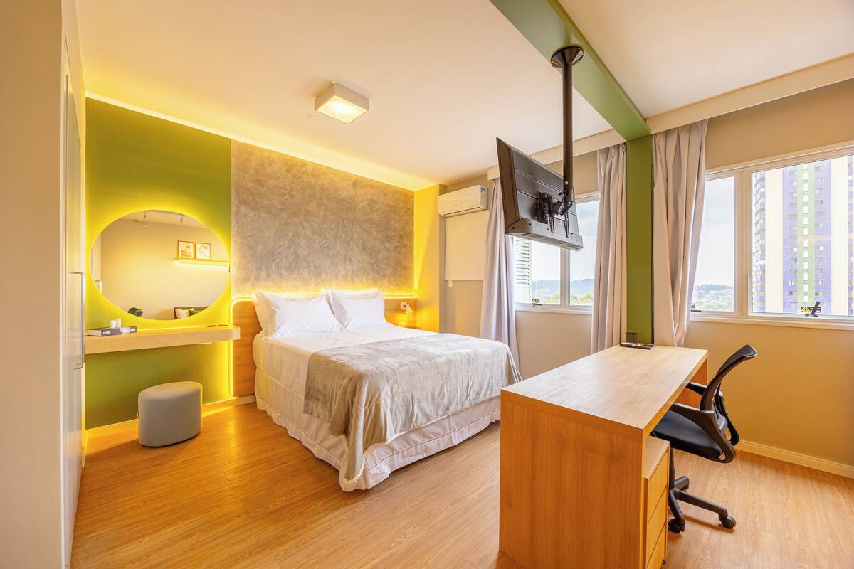 Une chambre d’hôtel moderne équipée d’un lit, d’un bureau, d’une télévision et d’une fenêtre donnant sur la ville.
