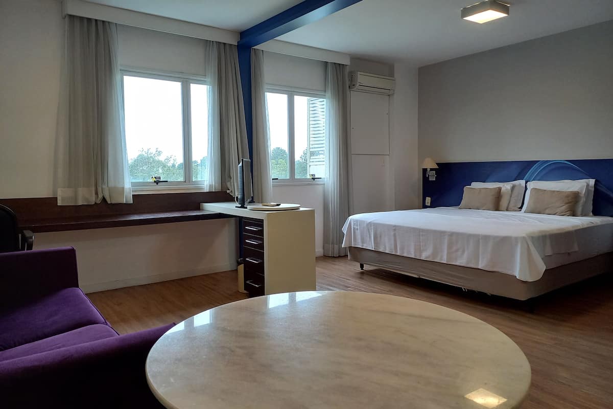 Une chambre d’hôtel avec un lit, un bureau avec une chaise, une table ronde et un fauteuil violet.