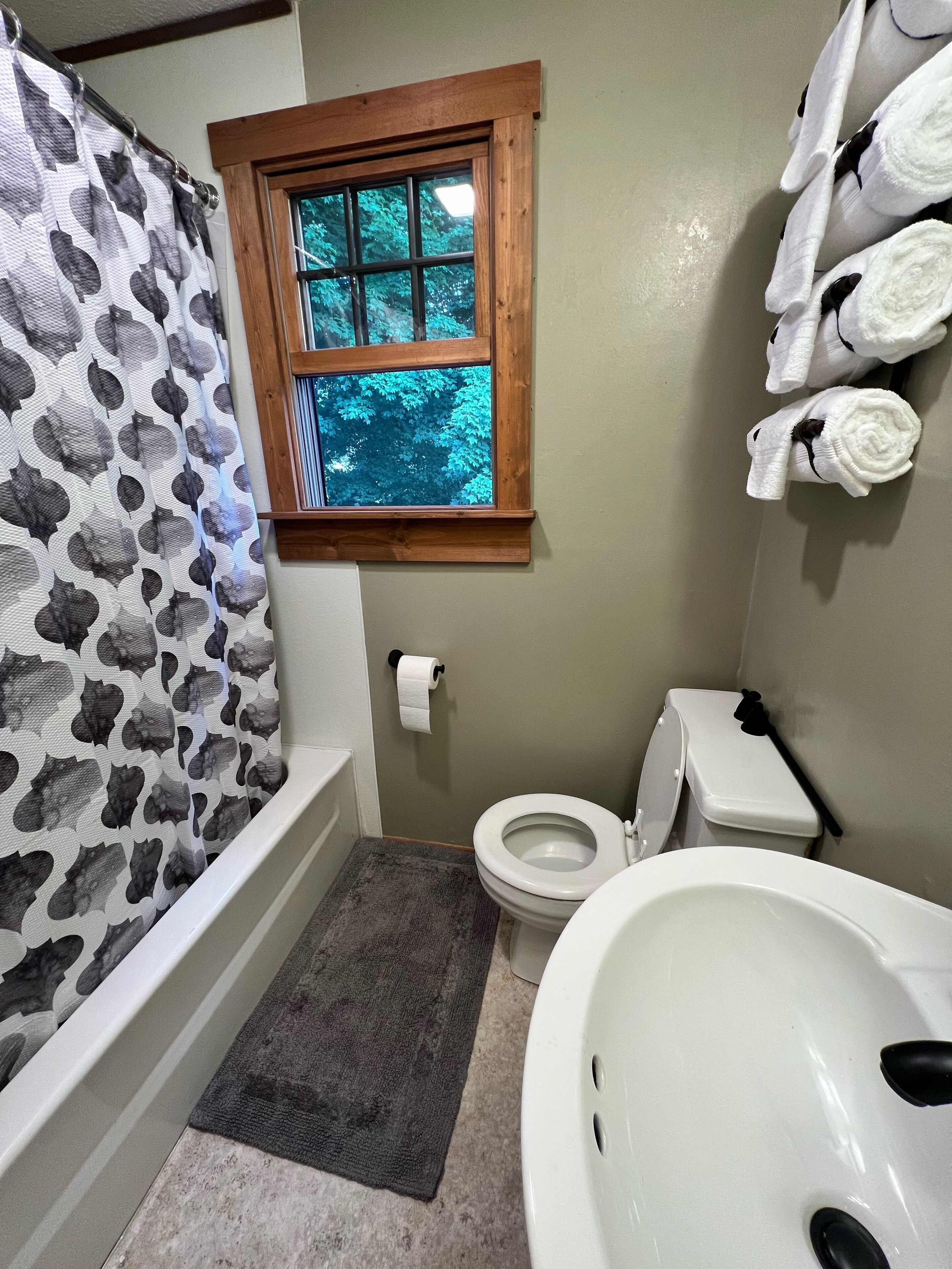 A bathroom with a shower curtain, a window, a toilet, and a sink.