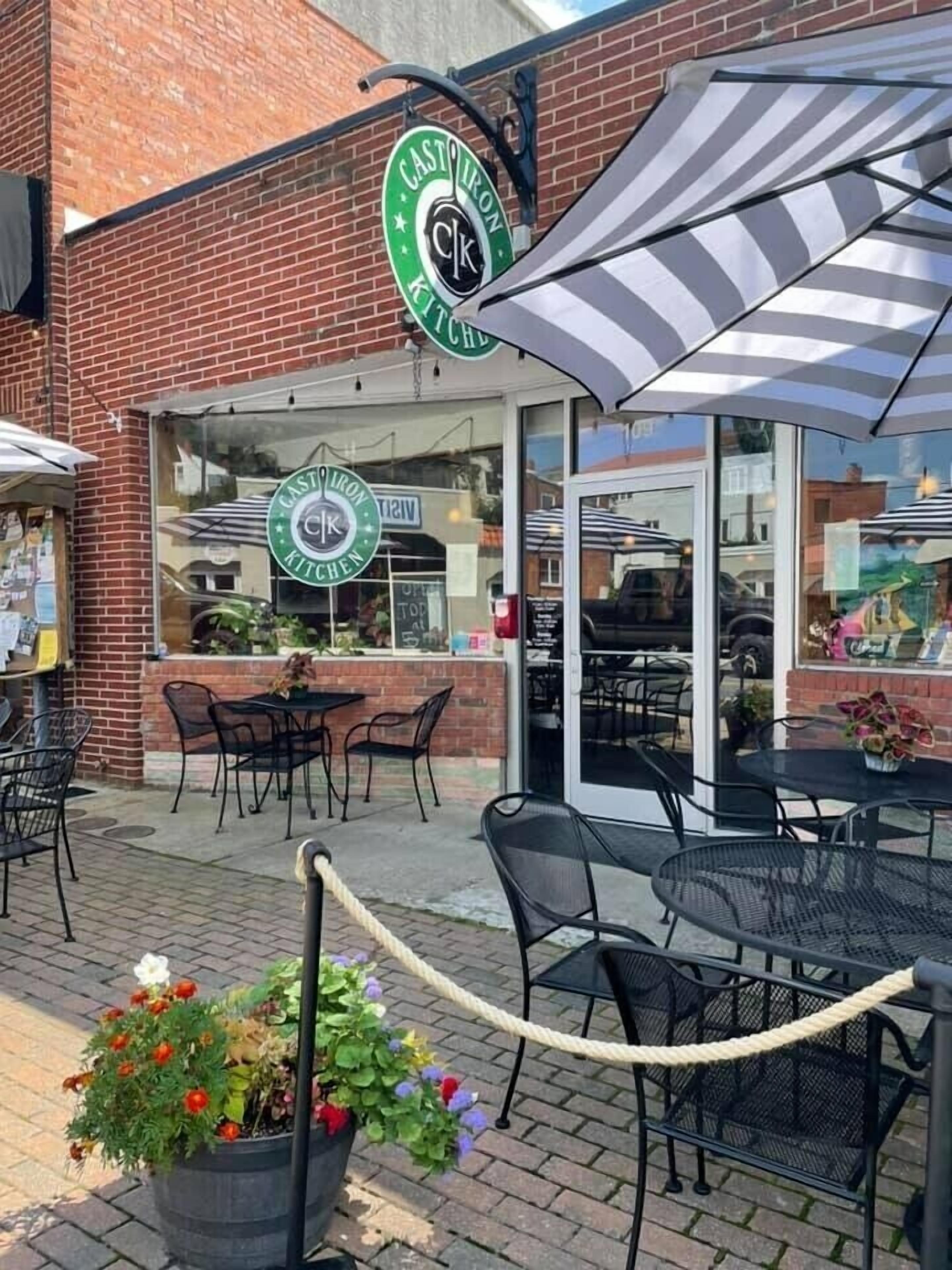 A brick building with a green sign reading "CAST IRON KITCHEN" and outdoor seating with umbrellas.