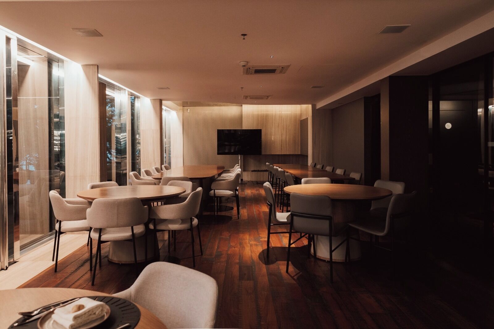 A modern conference room with glass walls, wooden flooring, and a flat-screen TV.