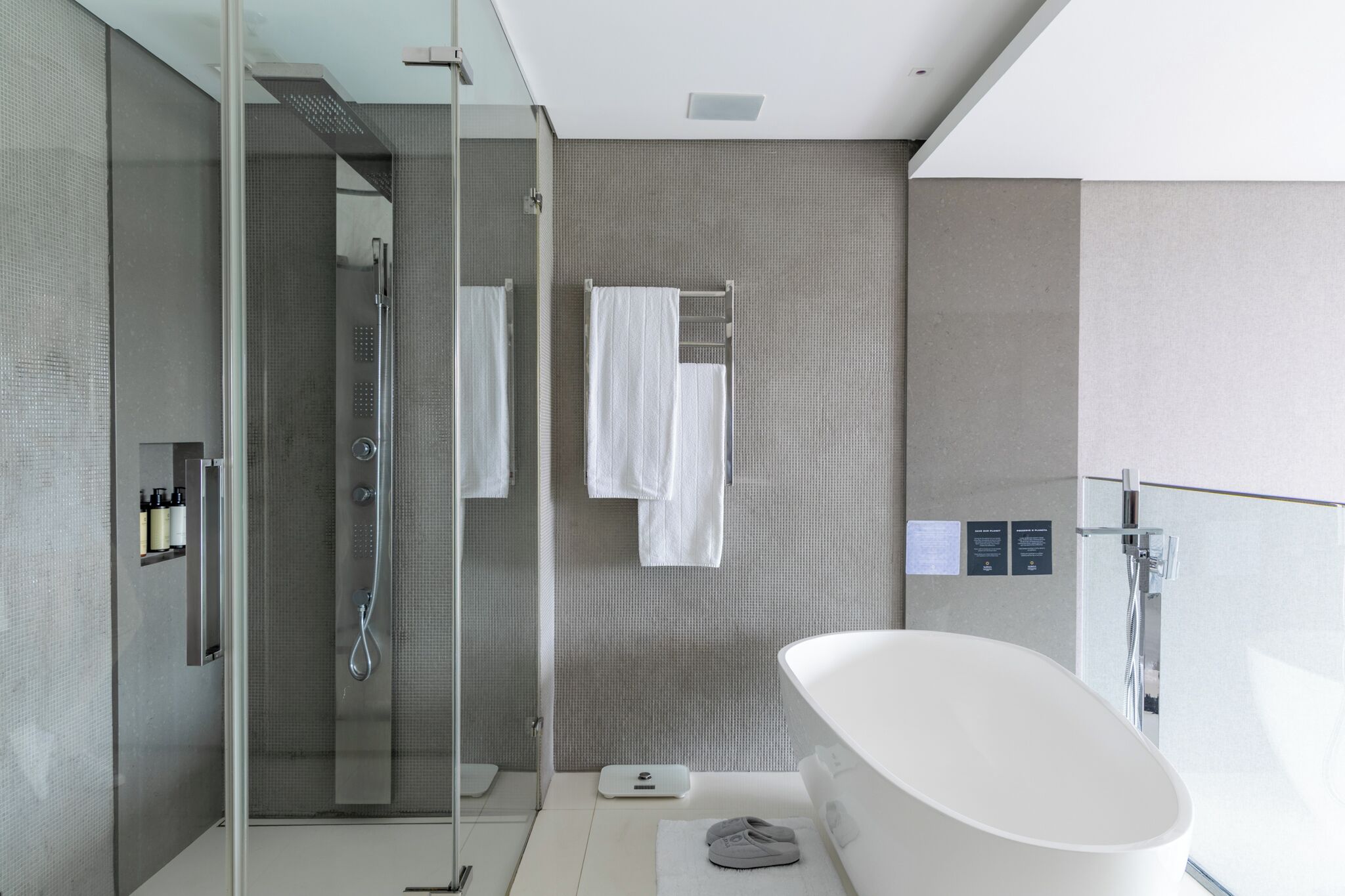 A modern bathroom with a glass-enclosed shower, a freestanding bathtub, and a towel rack with two white towels.