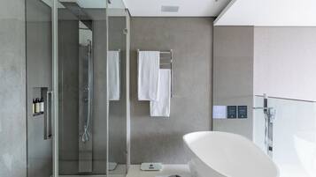A modern bathroom with a glass-enclosed shower, a freestanding bathtub, and a towel rack with two white towels.