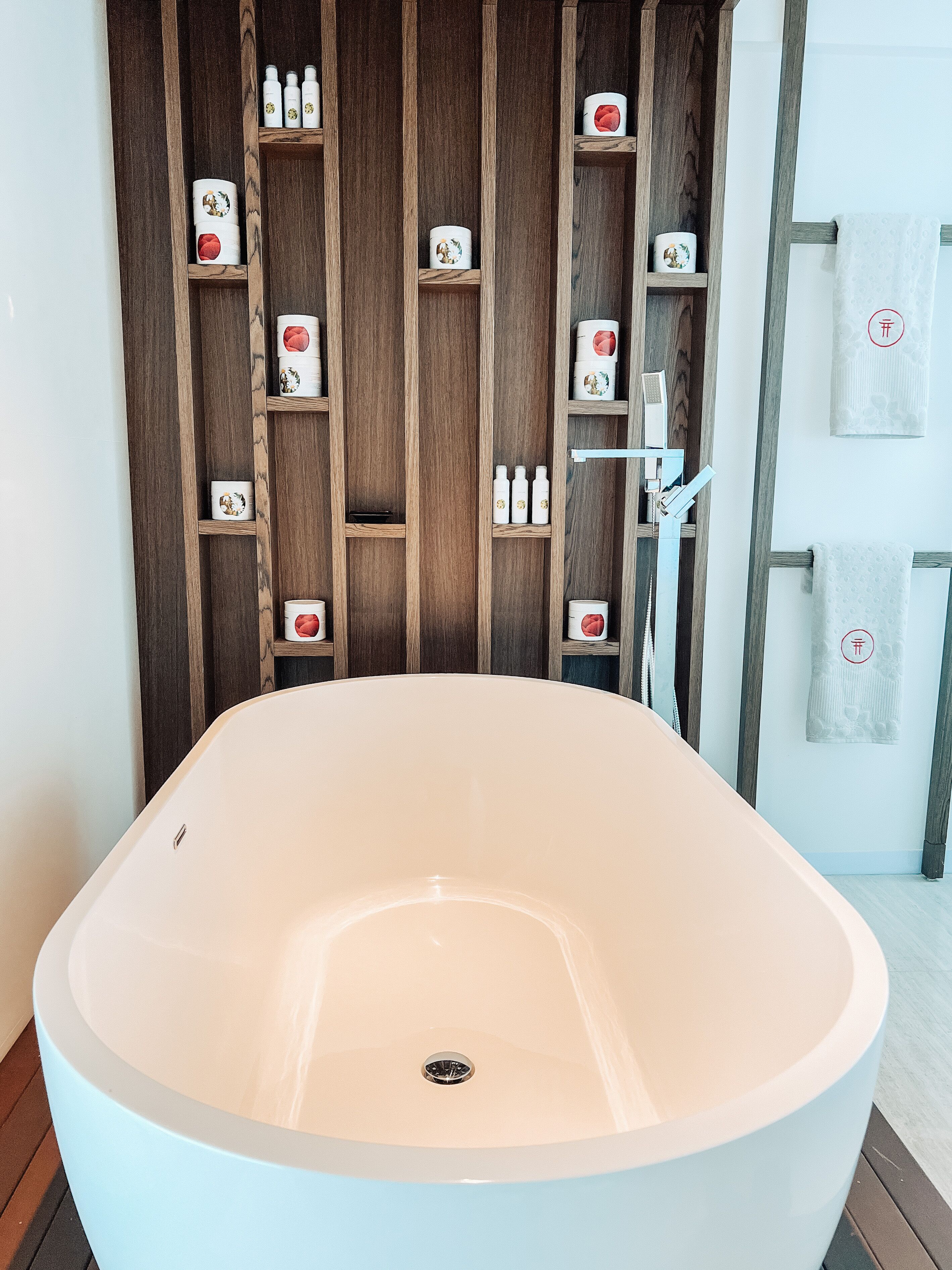 Un baño moderno con una bañera independiente, estantes de madera con artículos de aseo y un perchero para toallas.