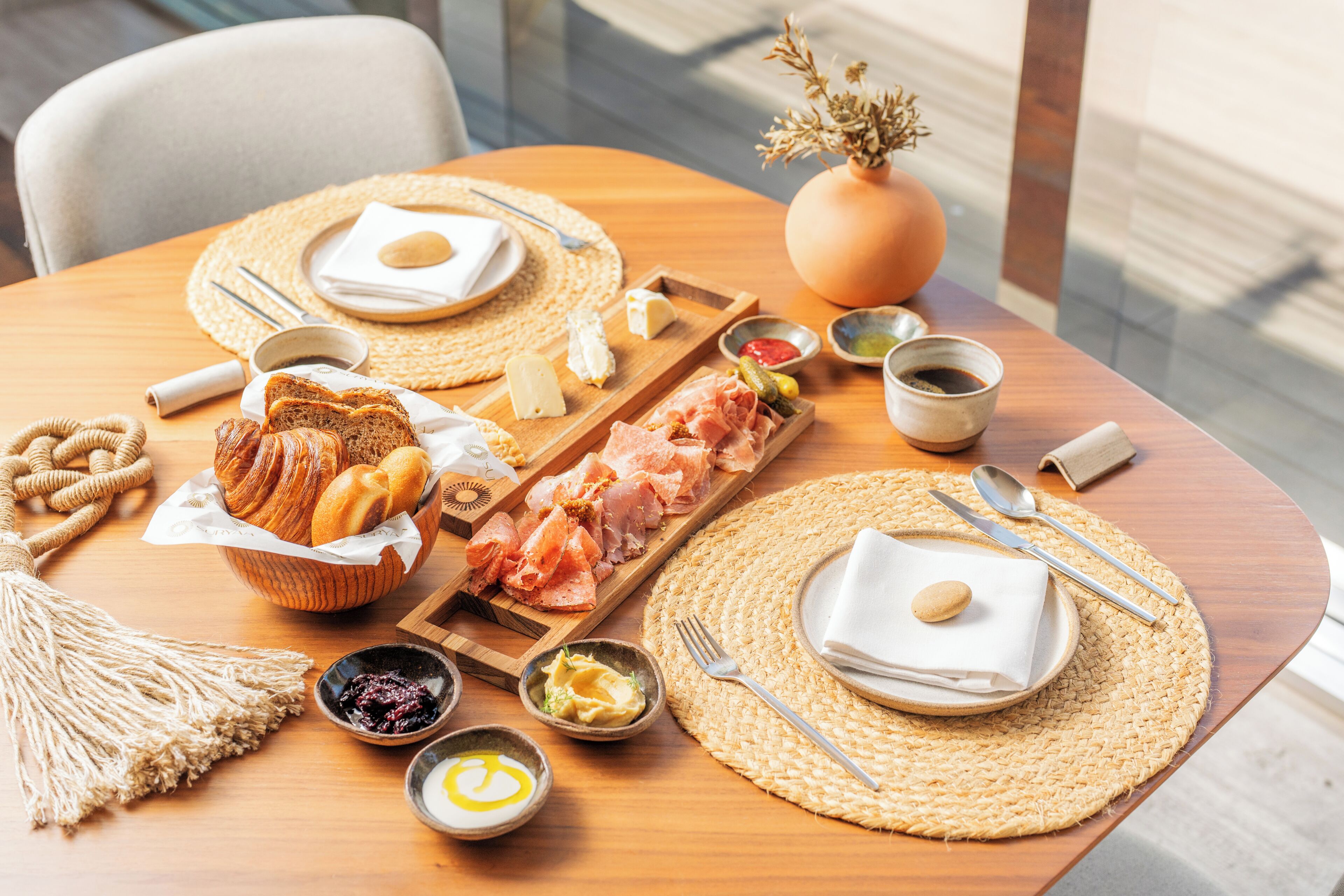 A breakfast setting with bread, pastries, meats, and condiments on a wooden table.