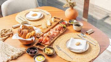 Un esmorzar amb pa, pastissos, carns i condiments damunt d'una taula de fusta.