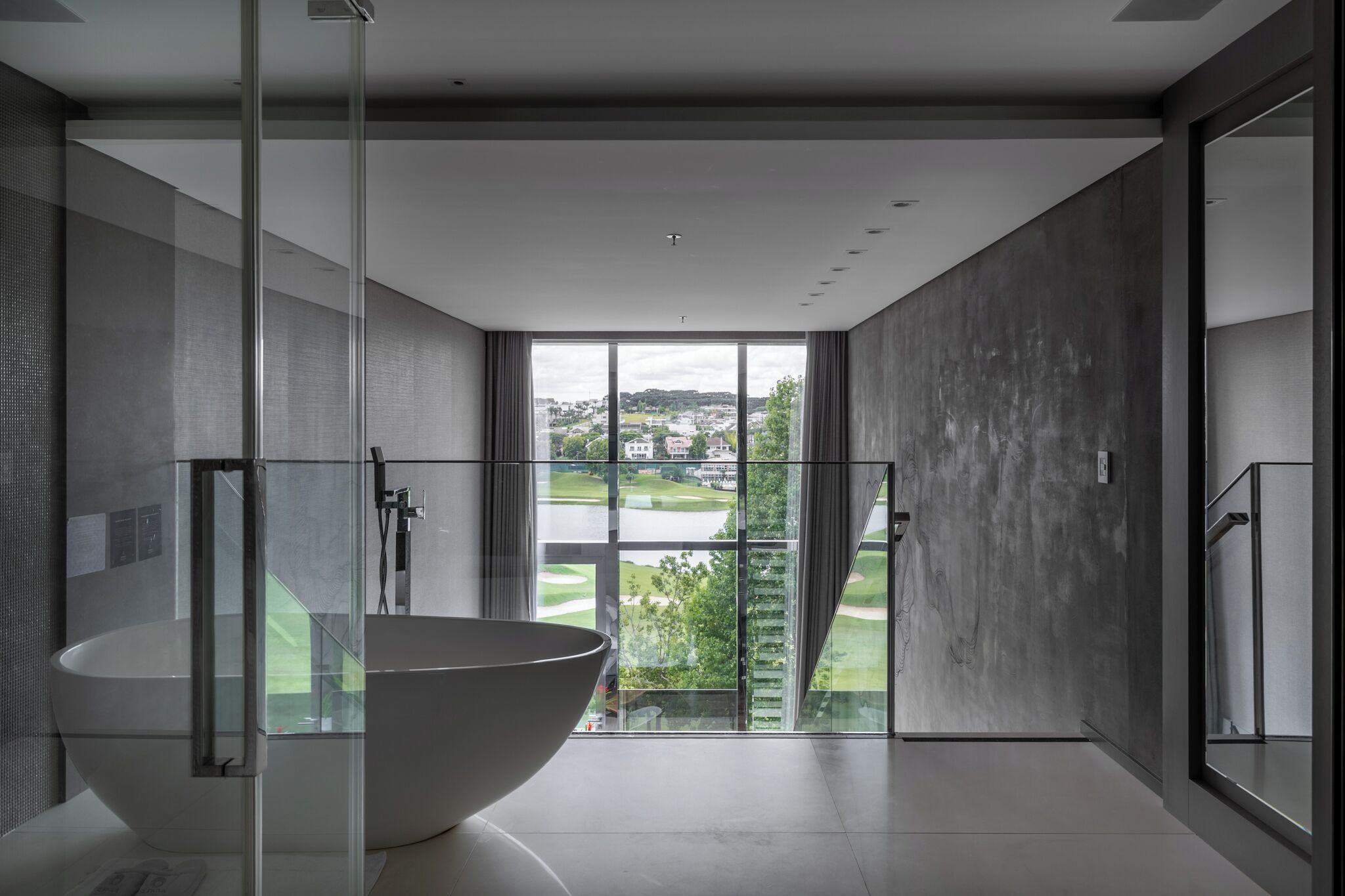A modern bathroom with a large glass-enclosed shower, a freestanding bathtub, and a view of a golf course through large windows.