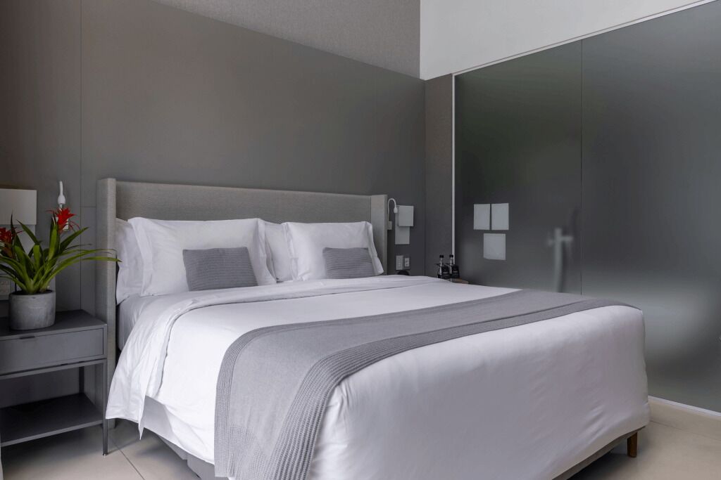 A modern bedroom with a large bed, a bedside table with a lamp, and a potted plant.