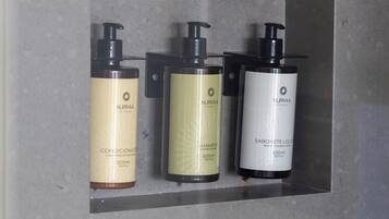 Tres ampolles de xampú i condicionador Surya dins d'una dutxera amb revestiment de rajoles grises.