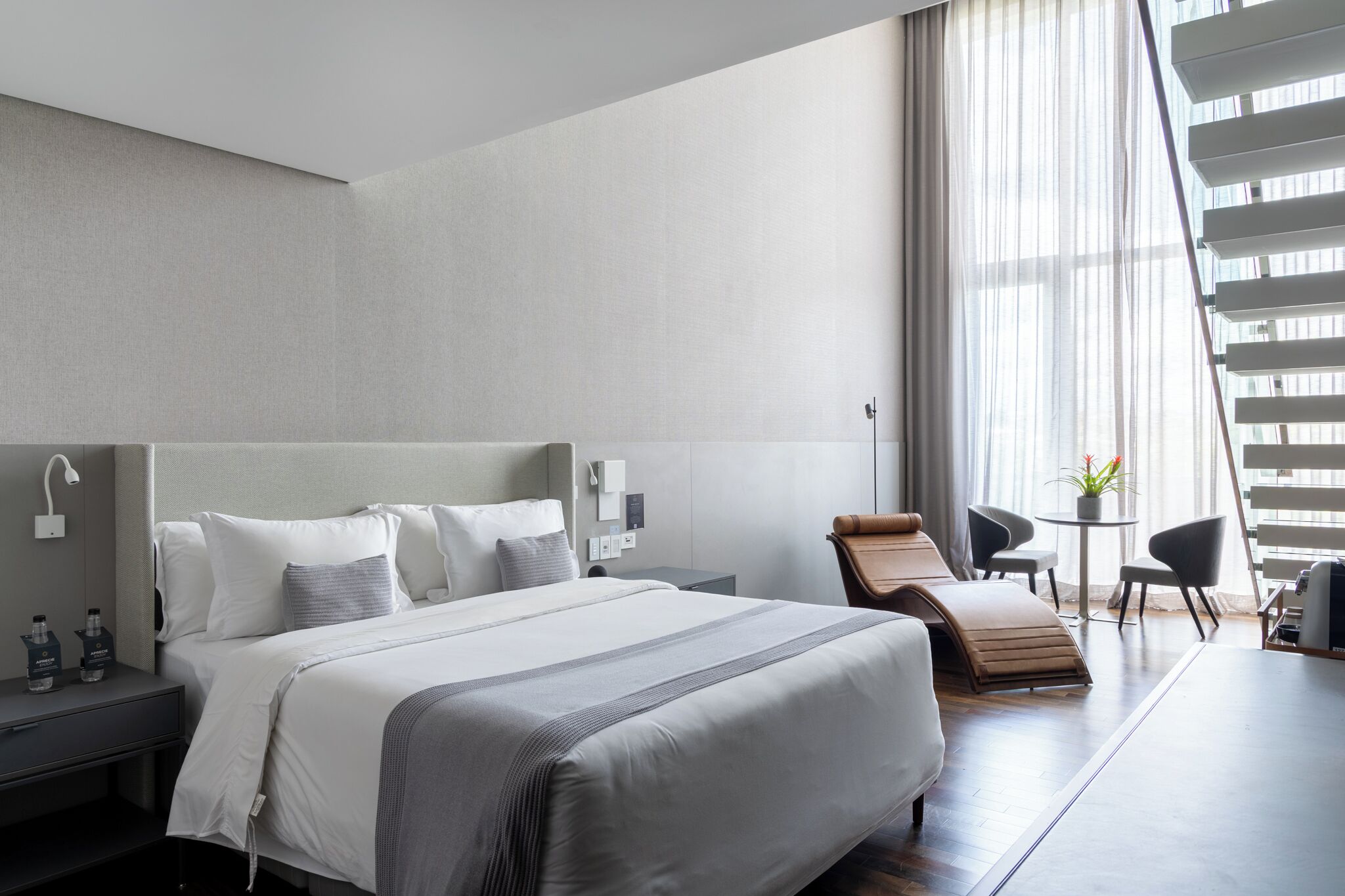 A modern hotel room with a large bed, a desk, a chair, and a small table with a plant.