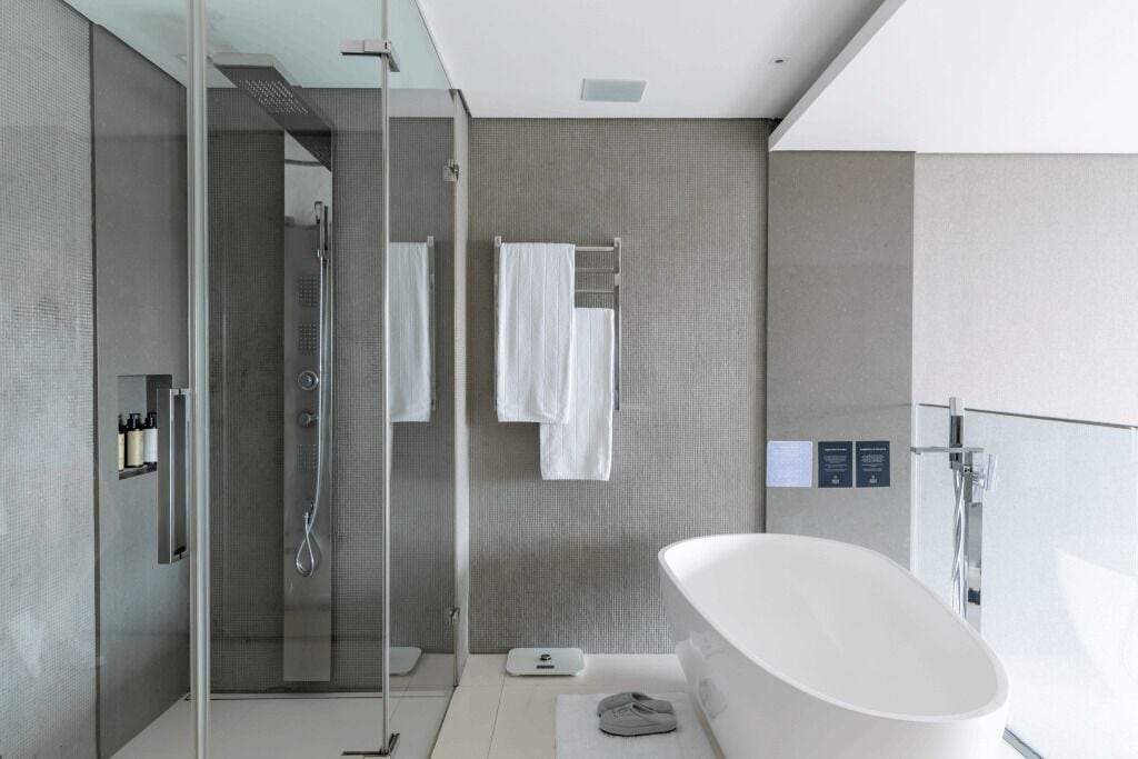 A modern bathroom with a glass-enclosed shower, a freestanding bathtub, and a towel rack with multiple towels.