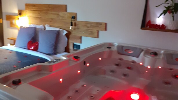 Une chambre avec une tête de lit en bois, un lit avec des oreillers, un tableau encadré au mur et un jacuzzi avec des lumières rouges.