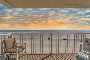 Un balcon donnant sur la plage, avec une balustrade blanche et deux chaises.
