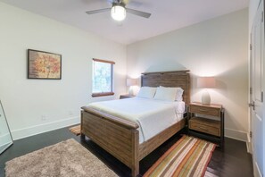 Quarto com cama de madeira, mesas de cabeceira, ventilador de teto, janela com persianas e tapete.