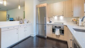 A modern kitchen with white cabinetry, stainless steel appliances, and a dark wood floor.