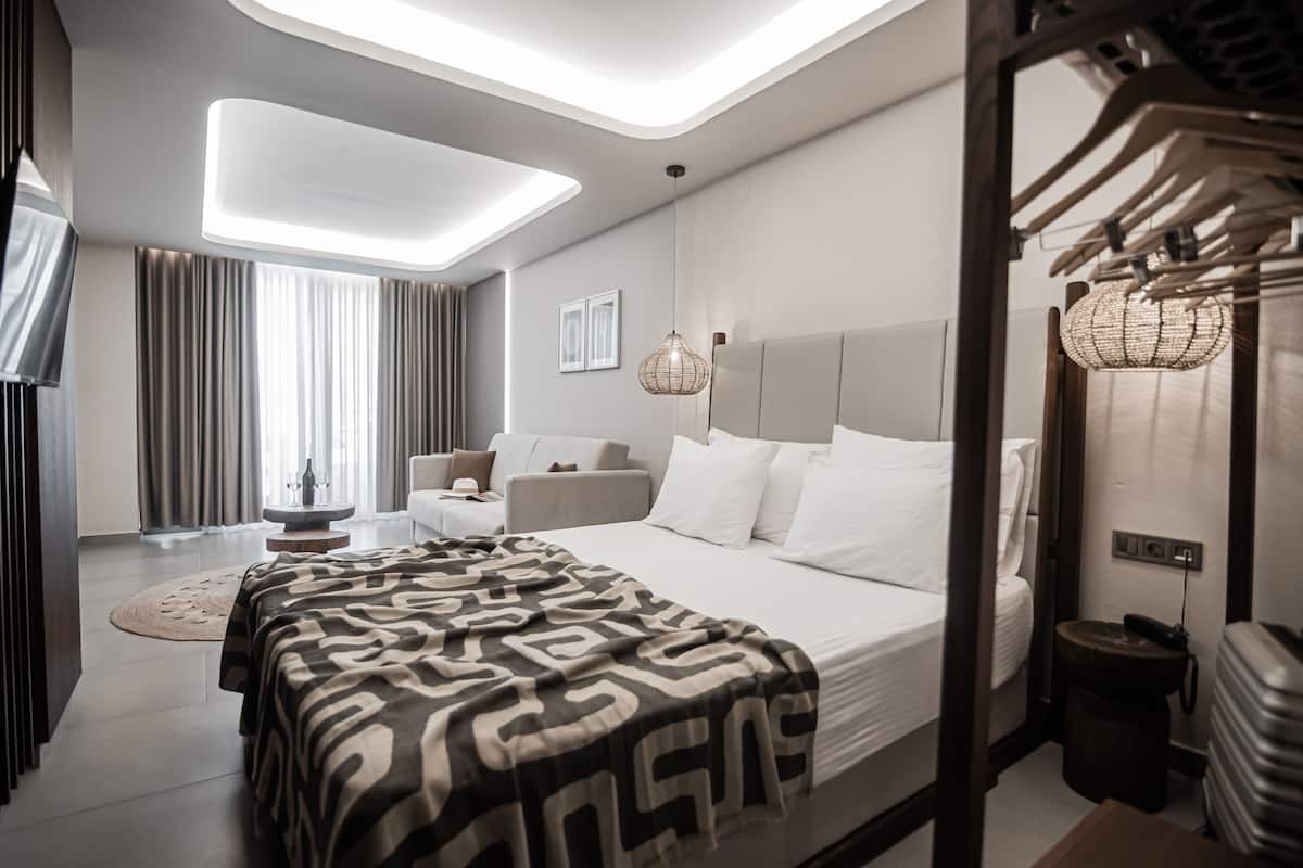 A modern hotel room with a large bed, a round coffee table, a sofa, and a dining table.