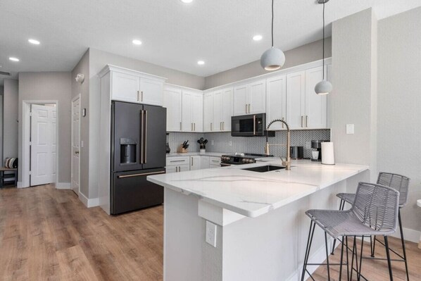 A modern kitchen with white cabinetry, a large island, stainless steel appliances, and pendant lighting. - Exquisite Escape At Windsor Hills with Pool (Kissimmee)